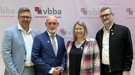 Gruppenfoto von Männern und Frauen vor einem Logo-Aufsteller