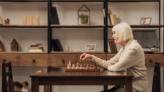 selective focus of senior woman sitting at table and playing chess in living room