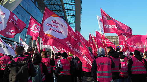 Menschen demonstrieren mit pinken Fahnen auf einem öffentlichen Platz.