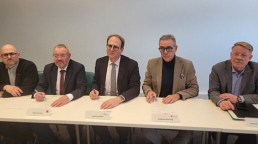 Mehrere Männer sitzen an einem langen Tisch und unterzeichnen Verträge