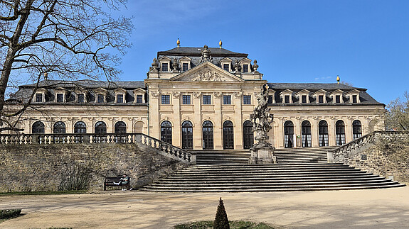 Ein barocker Palast mit blauem Himmel im Hintergrund und einer Parkanlage im Vordergrund