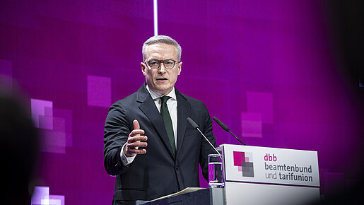 Ein Mann steht auf einer Bühne hinter einem Rednerpult und spricht in ein Mikrofon. Es handelt sich um Karsten Wildberger, Bundesminister für Digitales und Staatsmodernisierung