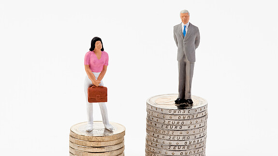 Kreutz: „Der Arbeitsmarkt muss attraktiver sein als der Heiratsmarkt“ Das Foto zeigt eine männliche und eine weibliche Figur, die auf Münzstapeln stehen. Der Stapel der männlichen Figur ist deutlich höher.
