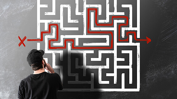 IT-Ausbildung im öffentlichen Dienst Junger Mensch steht vor einem an die Wand gezeichneten Labyrinth und denkt nach.
