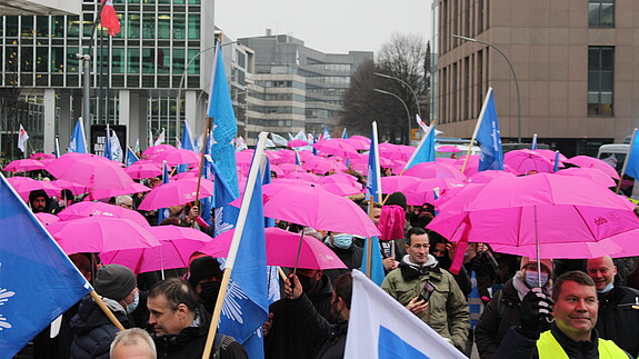 Es ist ein Demozug zu sehen, auf dem viele pinke Regenschirme gespannt wurden.