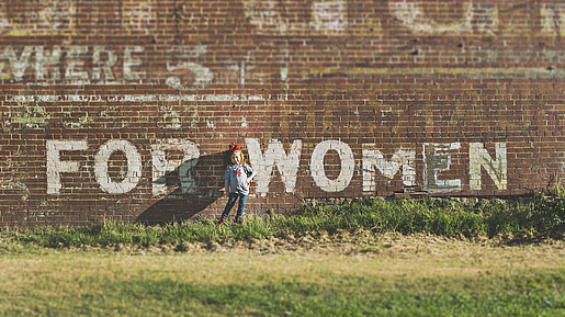 Ein Mädchen steht vor einer Wand auf der For Women steht