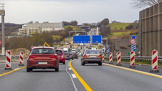 Zu sehen sind Autos auf einer Autobahn, rechts und links am Fahrbahnrand stehen Baustellen-Barken.
