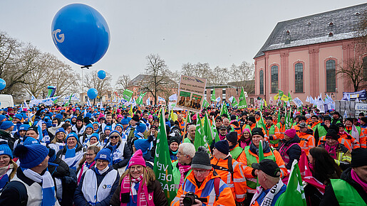Eine Gruppe Menschen mit bunten Warnwesten und Bannern demonstriert auf einem öffentlichen Platz