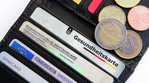Das Bild zeigt eine Geldbörse mit einer Gesundheitskarte, Ausweisdokumenten und Münzen.