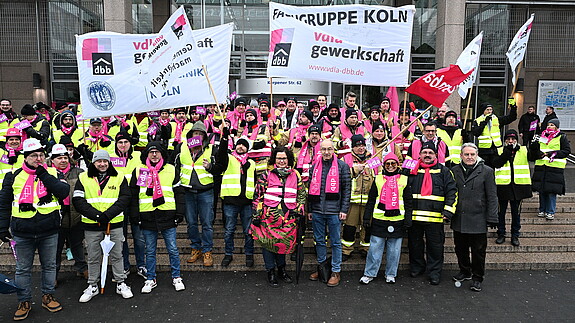 Eine Gruppe Menschen demonstriert mit bunten Bannern und Fahnen auf den Stufen eines Krankenhauses