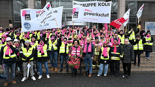Eine Gruppe Menschen demonstriert mit bunten Bannern und Fahnen auf den Stufen eines Krankenhauses