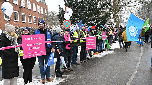 Menschen mit pinken Schildern und Warnwesten stehen als Menschenkette entlang einer langen Straße