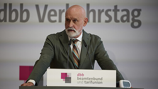 Ein Mann in Anzug steht hinter einem Rednerpult und spricht in ein Mikrofon