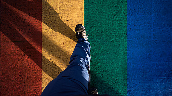 IDAHOBIT Eine Person geht über eine asphaltierte Straße, die in den Regenbogenfarben angemalt ist.