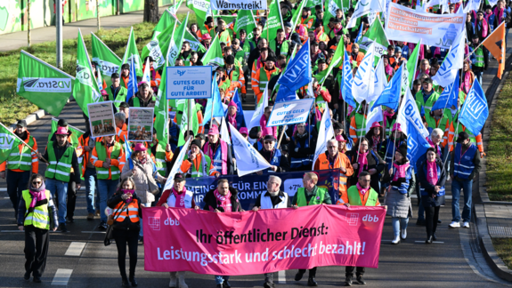 Luftaufnahme von einer Gruppe Menschen, die mit bunten Fahnen und Warnwesten auf einer Straße demonstrieren