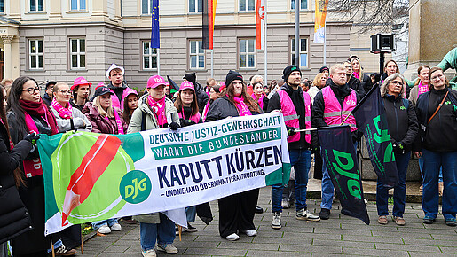 Eine Gruppe Menschen demonstriert mit Bunten Bannern und Warnwesten auf einem Platz.