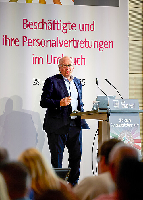 Ein Mann steht hinter einem Rednerpult und spricht zum Publikum