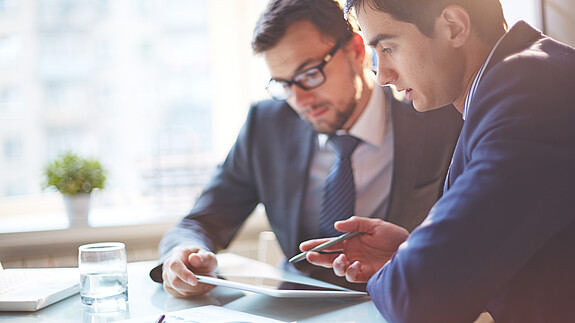 Zwei Männer im Büro sehen gemeinsam auf Tablet und besprechen sich