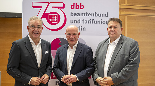 Drei Männer in Anzügen stehen vor einem Aufsteller und blicken in die Kamera