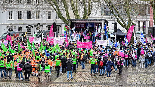 Eine Menschengruppe protestiert mit bunten Fahnen auf einem öffentlichen Platz.