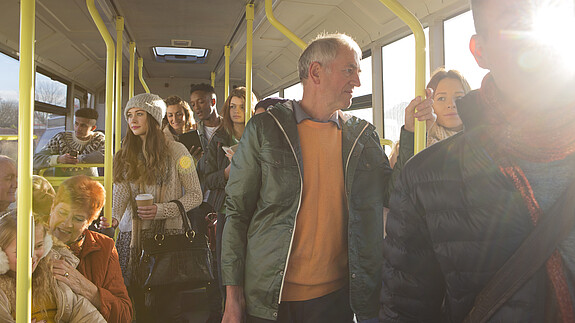 Blick in den Innenraum eines Busses auf stehende und sitzende Passagiere aus allen Altersgruppen