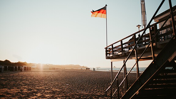 Tag der deutschen Einheit An einen Stelzenhaus am Strand ist die Deutschlandflagge gehisst, im Hintergrund scheint die Abendsonne.