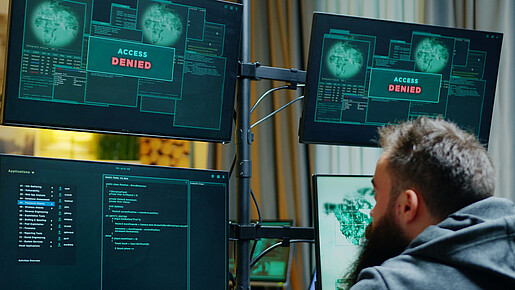 Cybersicherheit Ein Mann sitzt vor mehreren Computer-Monitoren, auf denen "Zugriff verweigert" zu lesen ist.
